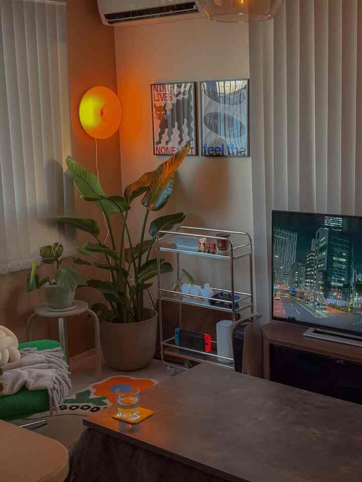 白い壁とオレンジ色の間接照明があるリビング、緑のソファとコーヒーテーブル、植物が配置された雰囲気のある空間