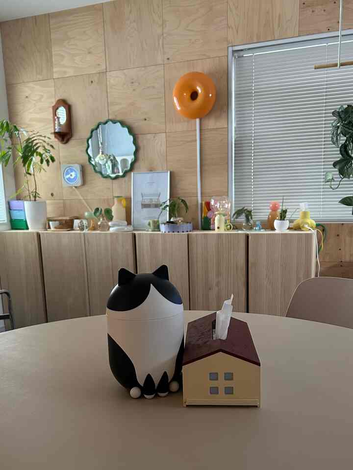 ナチュラルな木目調の壁とキャビネットがあるリビング、丸いテーブルの上に猫型のオブジェと小さな家のティッシュボックスが置かれた雰囲気のあるインテリア