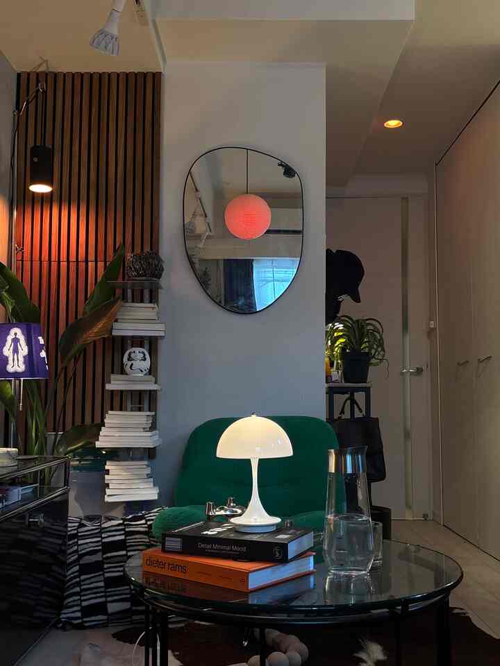 Modern long and narrow 1K studio with white walls and green armchair, featuring glass table with art books and Louis Poulsen lamp