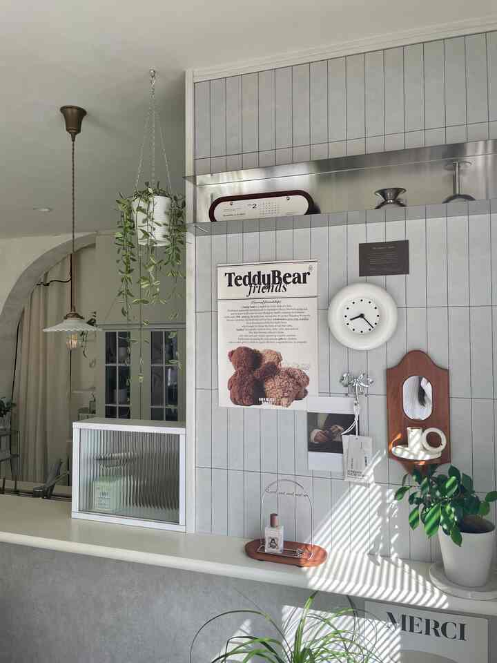 明るくナチュラルトーンのキッチン、腰壁にテディベアのポスターや小物がかわいらしく配置されたカフェ風インテリア