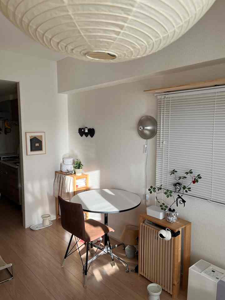 Cozy single household living space with natural wood flooring, white walls, round dining table, and wall sconce lighting