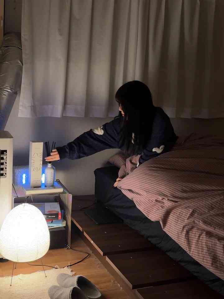 ライトブラウンとブラックのトーンの寝室、ベッド横のナイトテーブルにディフューザーとフロアランプが配置された雰囲気のあるインテリア
