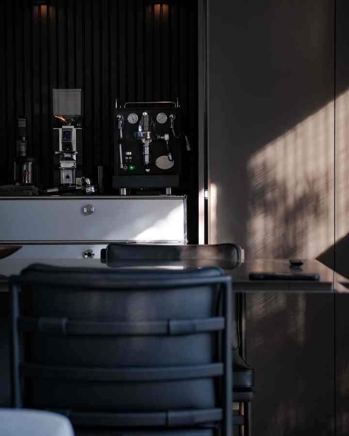 チャコールと黒を基調としたダイニングルーム、中央にエスプレッソマシンとグラインダーが配置された印象的なホームカフェ空間