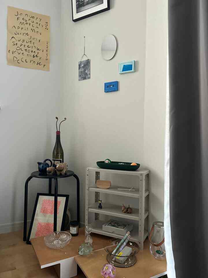 白い壁と木目調の床が特徴のワンルーム、ミニマルなテーブルやスツール、棚が配置された自然な雰囲気のインテリア