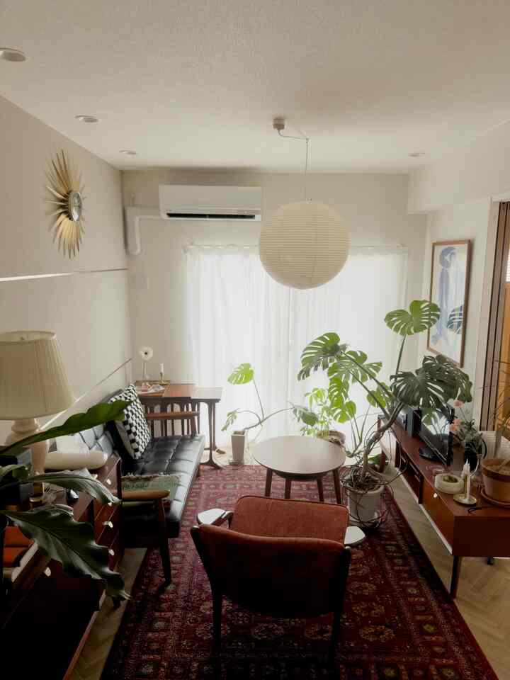 ブラウンの木目調と白い壁が調和するミッドセンチュリーモダンのリビング、モンステラの観葉植物と丸い和紙のペンダントライトが配置された落ち着いた雰囲気の空間