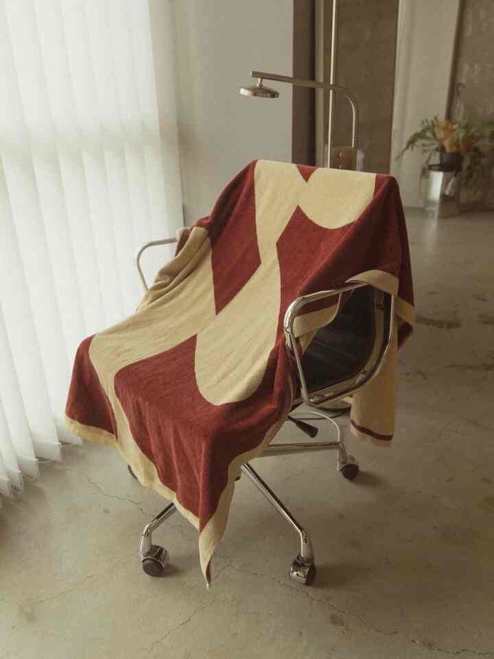 A red and ivory towel blanket draped over a chair in a minimally styled space with natural light.