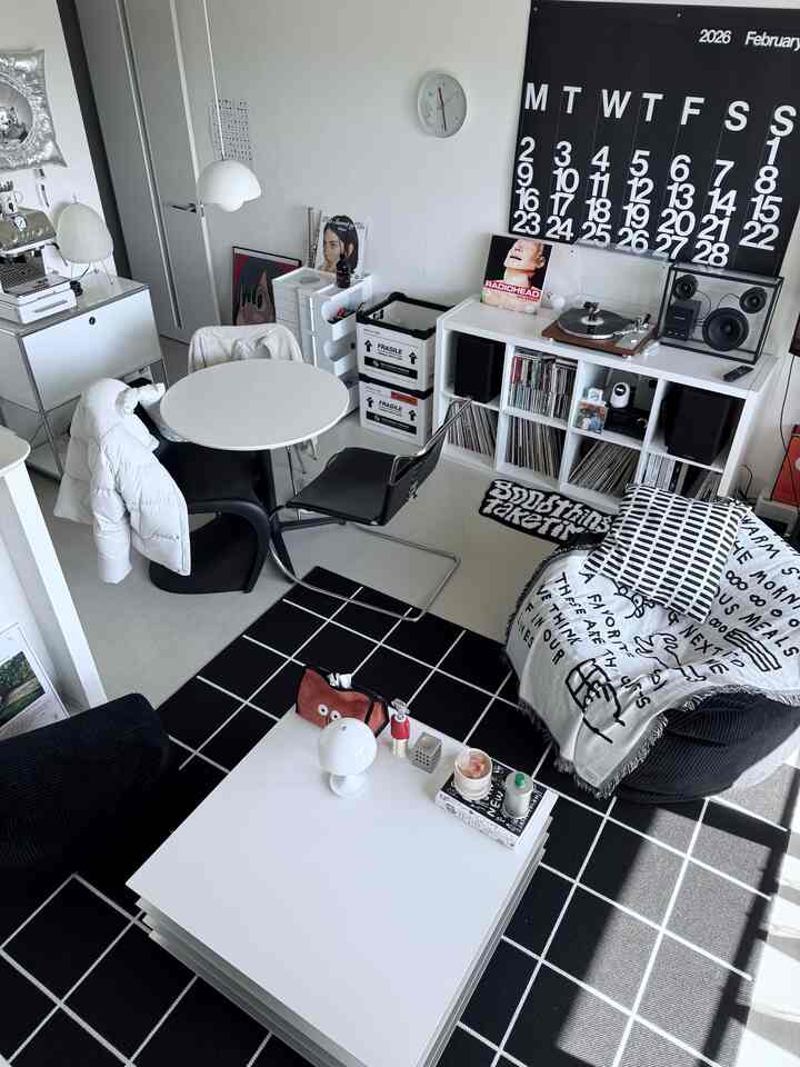 モノトーンのリビング空間。白と黒の家具とラグが配置され、音楽システムと時計がある印象的なインテリア