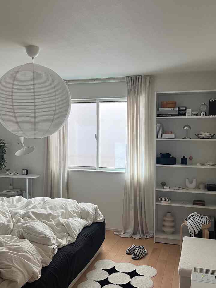 Monotone bedroom dominated by white and black colors, featuring a bed, rug, and shelving that create a natural and cozy atmosphere