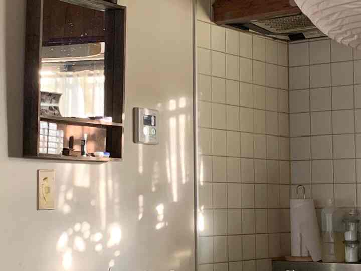 ベージュとホワイトのトーンの狭いキッチン壁面に木製フレームの鏡とタイルが配置されたヴィンテージ感のあるインテリア