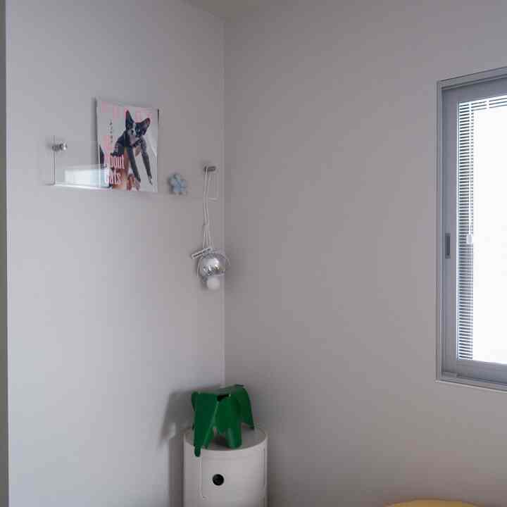 白い壁と透明なアクリル棚があるモダンなコーナースペース、緑のヴィトラ イームズ エレファントと銀色の壁照明が配置されたすっきりとしたインテリア