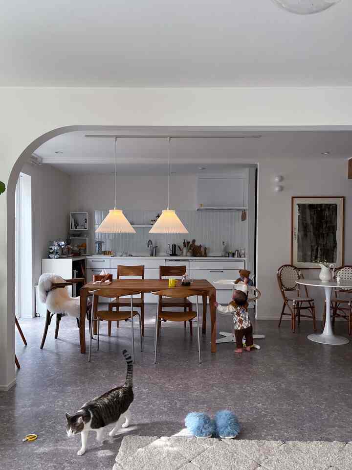 White and dark brown toned dining room and kitchen featuring vintage furniture, a child, and a cat in a cozy setting