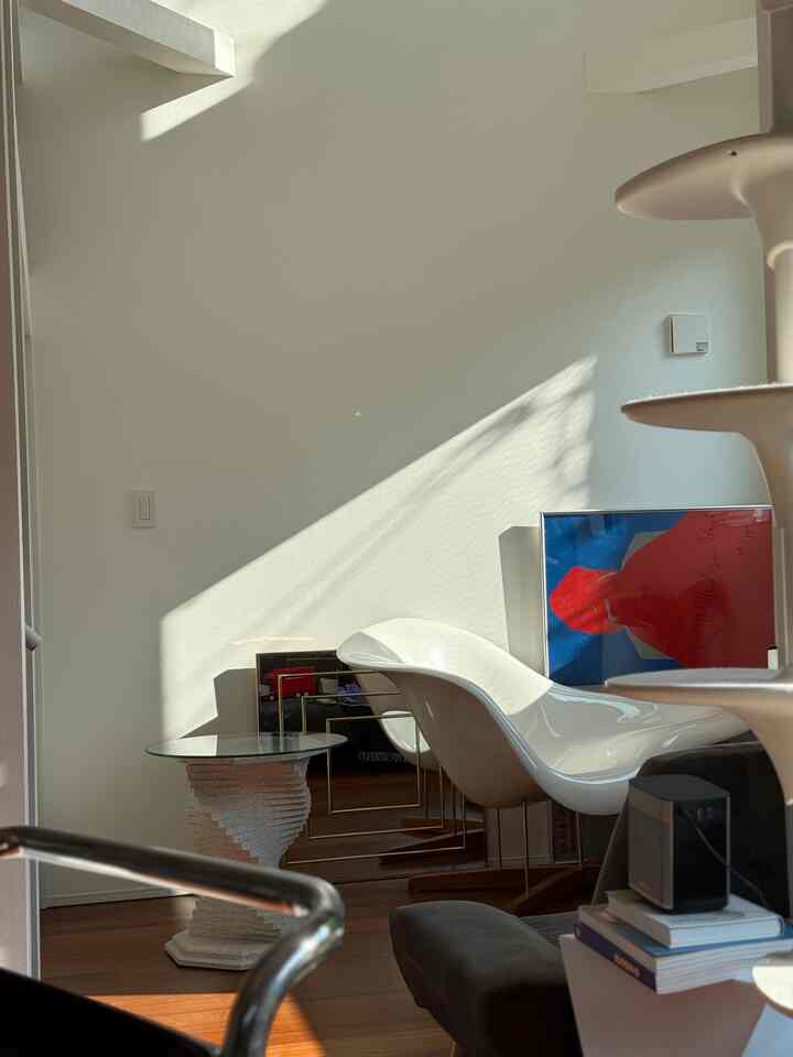 Living room with white walls and a mid-century modern lounge chair on warm brown wood flooring, bathed in natural sunlight