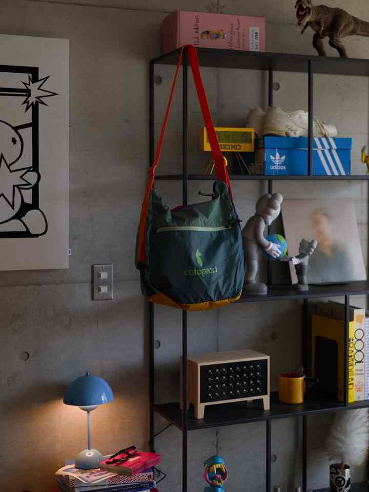 グレーのコンクリート壁とブルー・イエローのアクセントが効いたモダンな1LDK空間、金属製の棚にオブジェや本が並ぶ雰囲気のあるインテリア