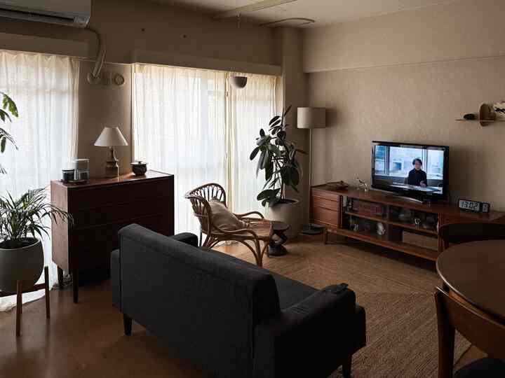 ナチュラルな色調のワンルームリビング、木目調の家具とラタンチェア、大きな植物が配置された雰囲気のある空間