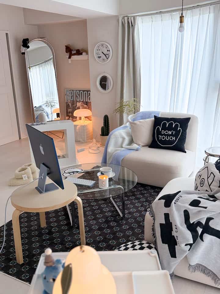 白と黒のトーンのリビング、モダンなソファと透明なコーヒーテーブル、ホームオフィス要素が配置された雰囲気のあるインテリア