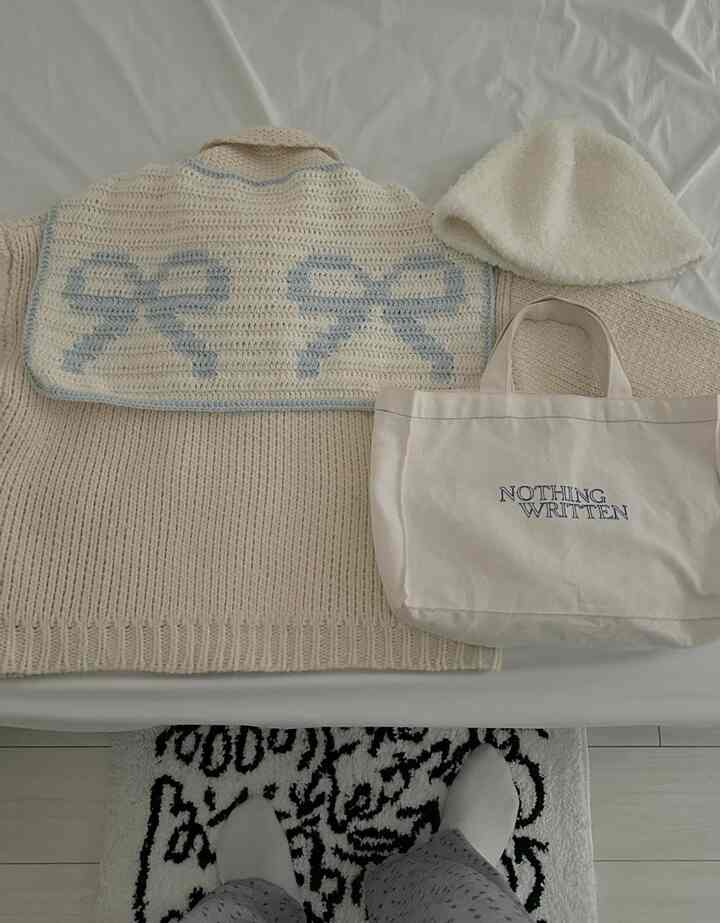 White and beige toned bedroom with knitwear and cream accessories placed on bed, presenting a natural ambiance