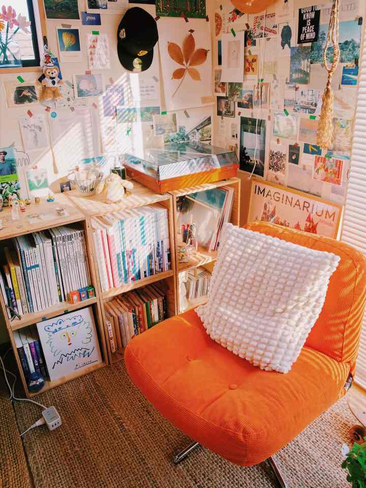 Warm natural tones small living room featuring an orange armchair, bookshelves, and a wall filled with framed art and posters creating a cozy atmosphere