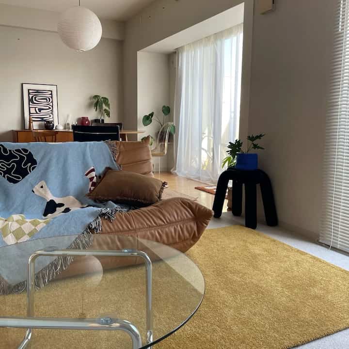 暖かいナチュラルトーンのリビング、黄色のラグとブラウンのソファが調和した雰囲気のある空間