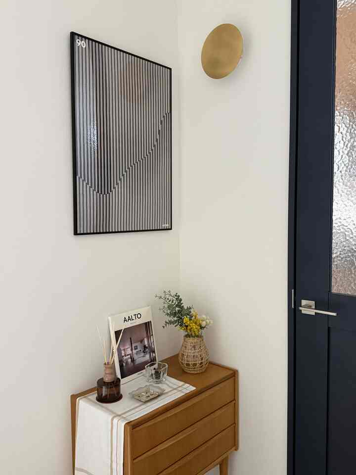 白い壁とネイビードアの玄関、木製のコンソールテーブルの上に花瓶とアルテックのポスターが配置されたシンプルな空間
