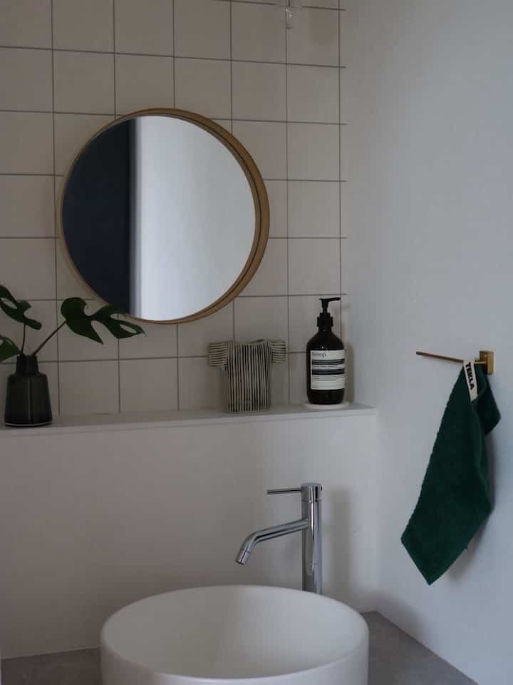 白とナチュラルウッドのトーンで統一されたシンプルなサブ洗面スペース、丸い鏡と緑のタオルが配された清潔感あるインテリア