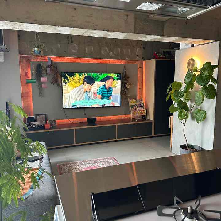 グレーのソファと黒のテレビ台が配置されたモダンなワンルームのリビング、コンクリートむき出しの天井が自然な雰囲気を醸し出すインテリア