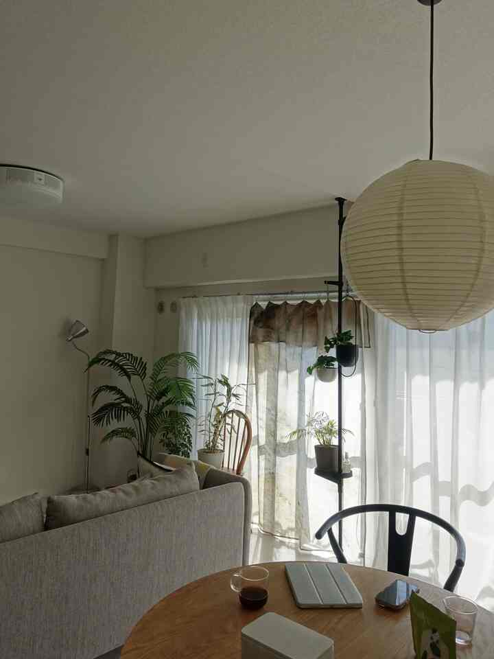 ナチュラルな色調のリビングとダイニング、ベージュのソファと木製のダイニングテーブル、ペンダントライトとカーテンが配置された雰囲気のある空間