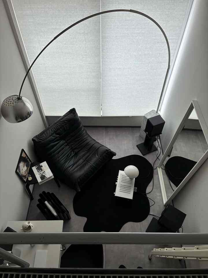 Monotone small living room featuring a black sofa, floor lamp, and a uniquely shaped black rug creating a simple, modern atmosphere