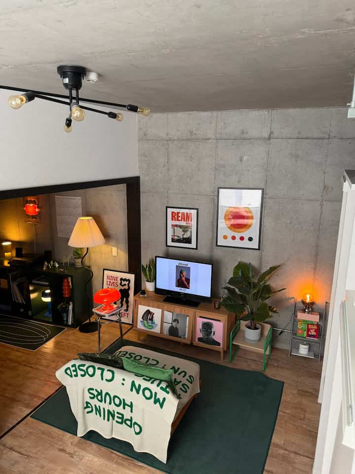 Living room with gray concrete wall and wooden floor, featuring green rug, sofa, and stylish lighting in mid-century modern style