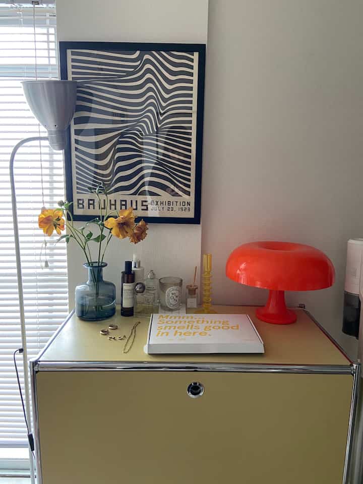 Mid-century modern living room with a yellow sideboard featuring a red table lamp and flower vase, topped by black and white Bauhaus art on the wall