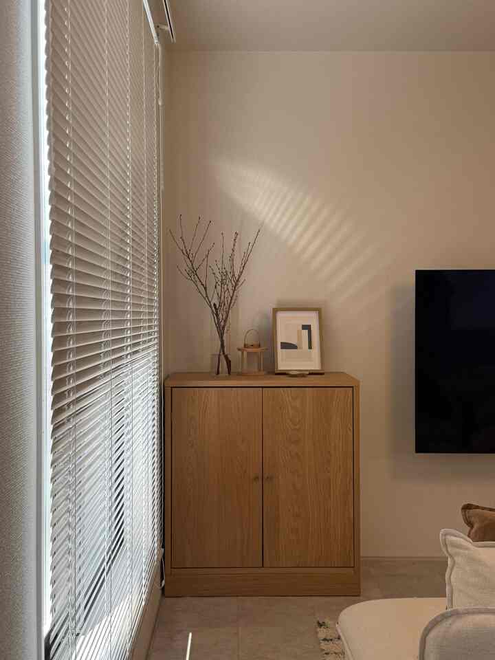 白とウッドトーンの調和が美しいモダンなジャパンディスタイルのリビング、すっきりとしたキャビネットとブラインドが配置された落ち着いた空間