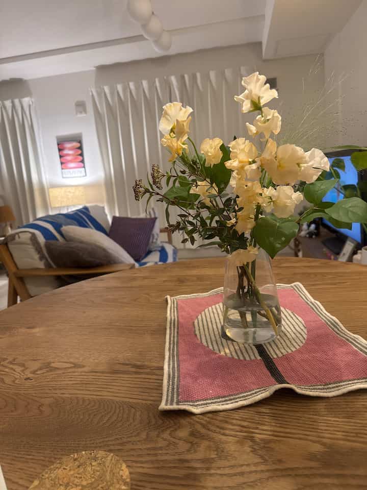 温かみのあるベージュとナチュラルウッド調のダイニング、中央に花瓶と花が置かれた木製テーブルが配置された雰囲気あるインテリア