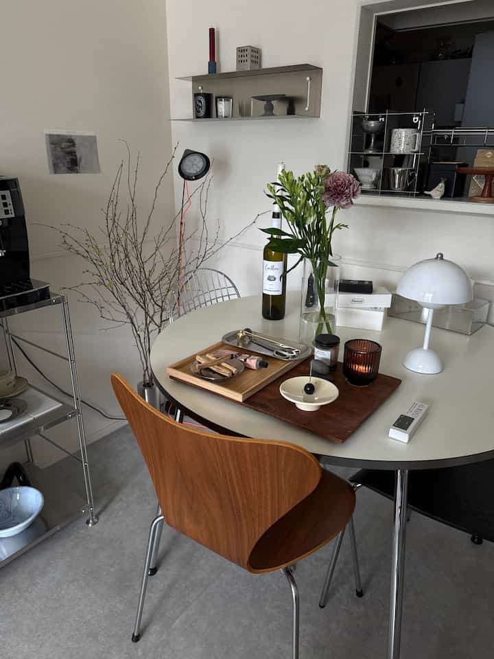 ホワイトトーンのミッドセンチュリーモダンなダイニングルーム、丸テーブルに木製の椅子や花瓶、キャンドルが配置された雰囲気のある空間