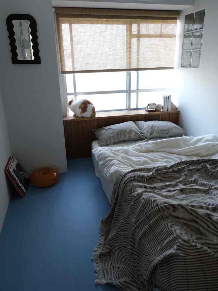 ナチュラルブラウンとブルーの床が特徴的小さな寝室、窓辺に猫がいて、落ち着いた雰囲気のあるインテリア
