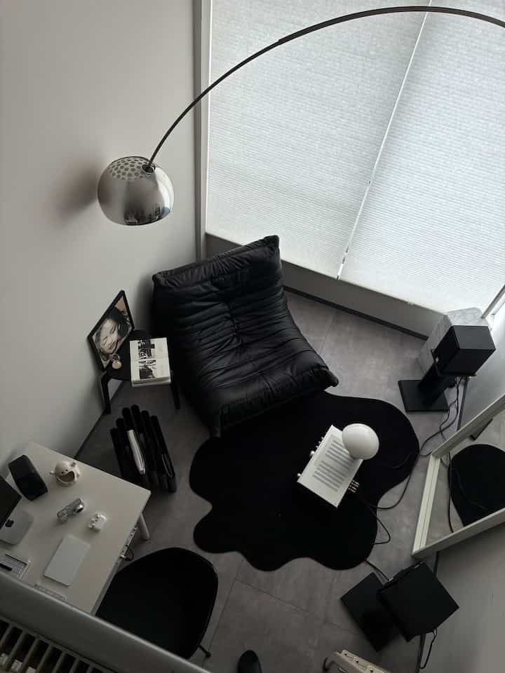 モノトーンの小さなリビングスペース、黒のアームチェアと不規則なラグ、アーチ型フロアランプが配置された落ち着いたインテリア