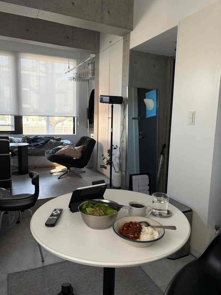 Monotone studio apartment dining space featuring a round table and armchair, creating a neat and practical breakfast area