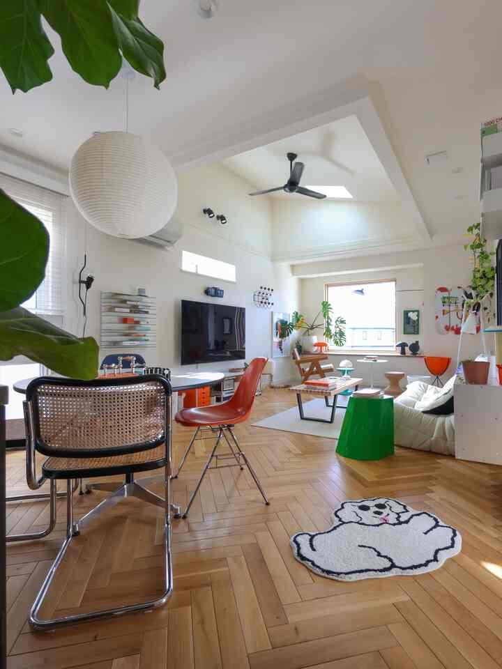 白を基調とした壁と天井、木目調の床が調和するミッドセンチュリーモダンのリビング。多様な椅子とコーヒーテーブル、大きな窓と観葉植物が配置された明るく開放的なインテリア