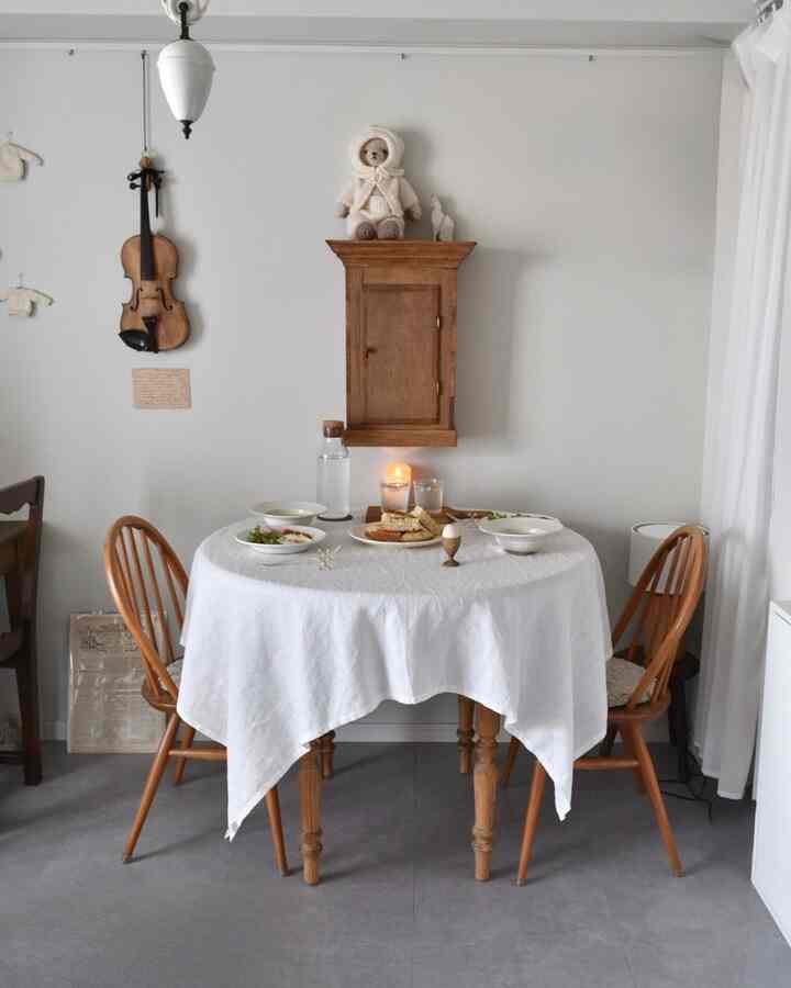 白い壁の1LDKダイニングルーム、木製のアンティーク家具とテーブルクロスがある円形テーブルが配置された落ち着いた雰囲気のインテリア