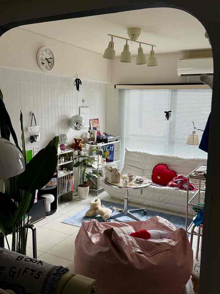 白とピンクのトーンが特徴の狭いリビング、低い家具とビーズクッション、植物が配置された雰囲気のある空間