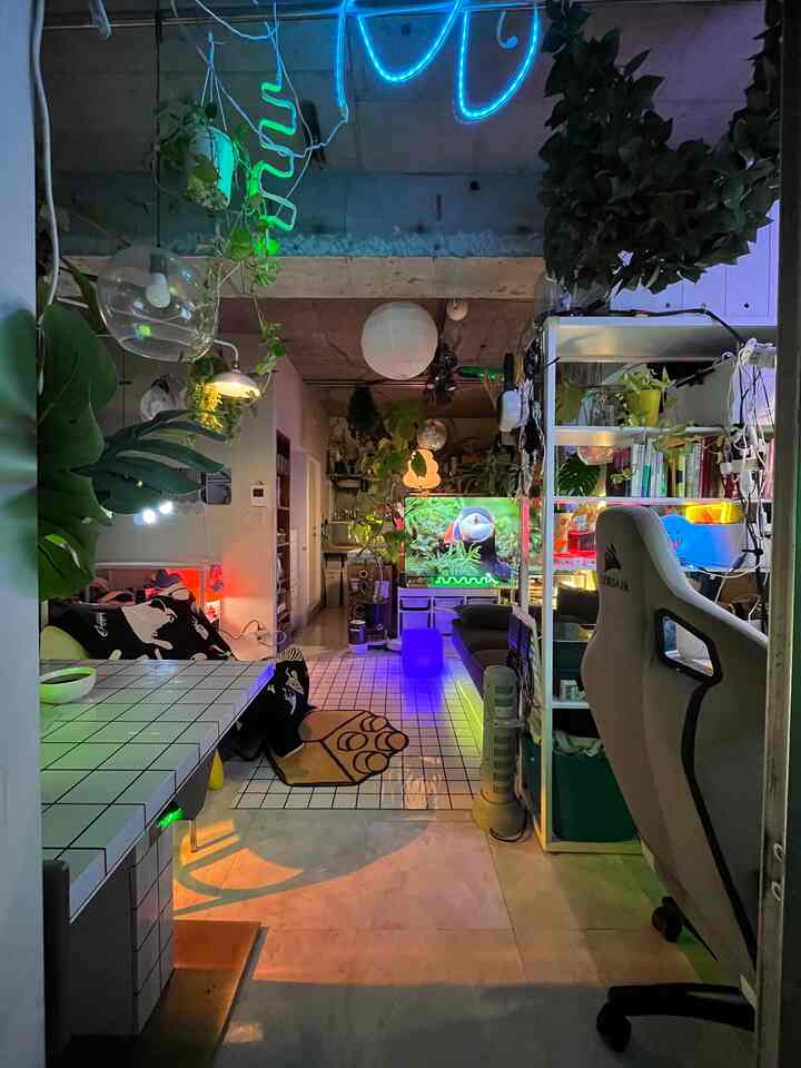 White and green toned studio apartment featuring a gaming chair and abundant leafy plants in a modern industrial space