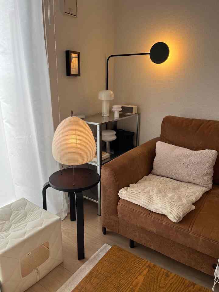 ナチュラルな色調の1LDKリビング、ブラウンのソファとスツール、猫用ハウスが配置された雰囲気のある空間