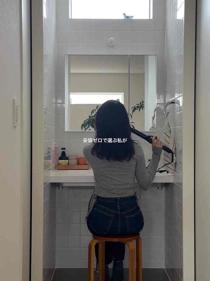 白いタイル壁と木製スツールが配置された清潔なバスルーム、中央に大きな鏡と洗面台がある雰囲気のあるインテリア