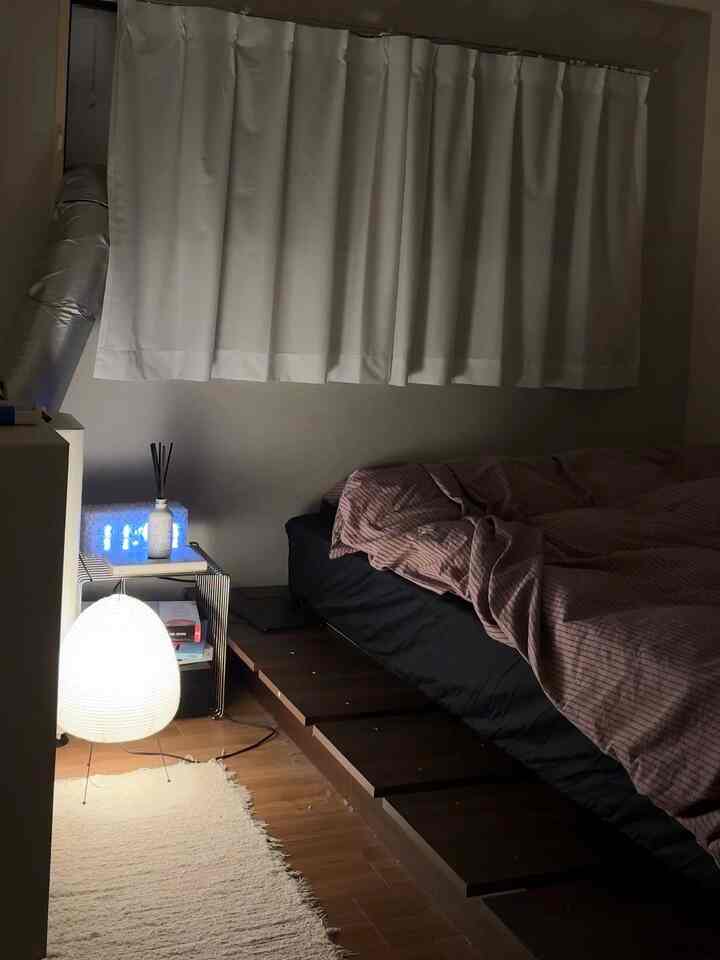 白いカーテンと茶色のベッドが配置されたナチュラルな色調の寝室、柔らかなラグと暖かい照明が印象的な空間