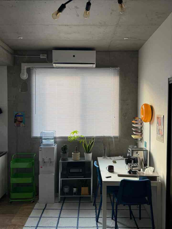 白とグレーのトーンの小さな空間、窓際に植物とすっきりとした家具が配置されたモダンでナチュラルなホームカフェのインテリア