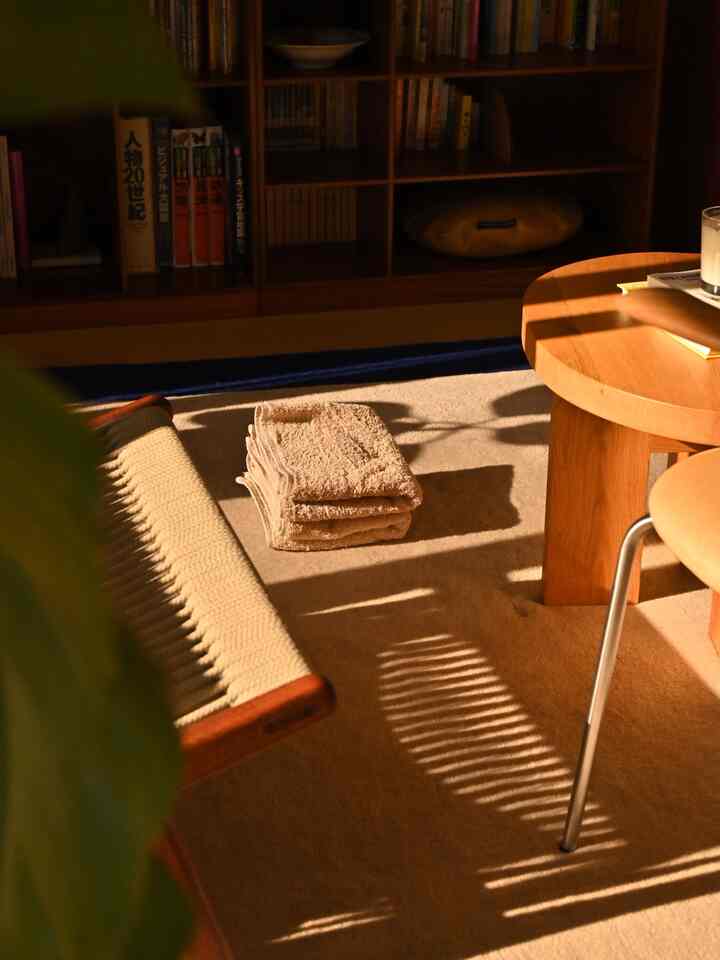 ベージュとナチュラル色調のリビング、中央に折りたたまれたタオルと木製サイドテーブルが配置された温かみのあるインテリア