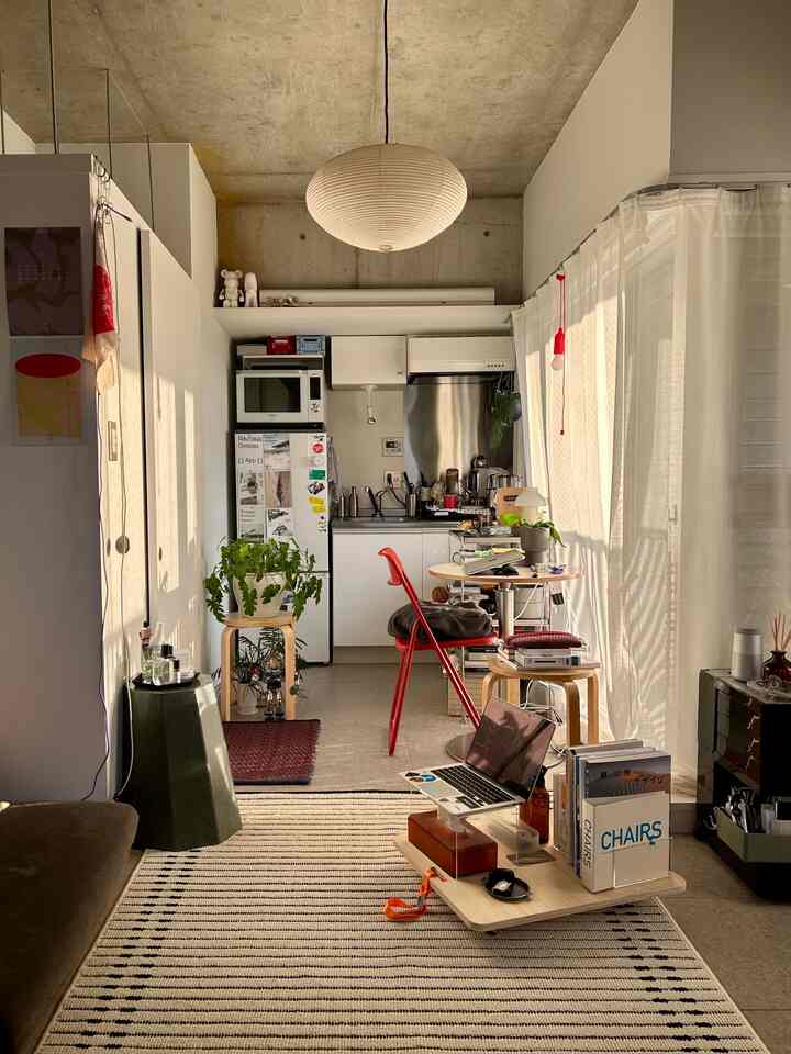 White and brown-toned studio apartment living room and kitchen with a red folding chair and striped rug, creating a cozy atmosphere