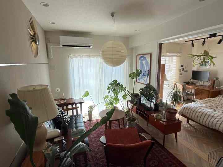 白を基調としたミッドセンチュリーモダンの1LDKリビング、観葉植物と木製家具が配置された温かみのある空間