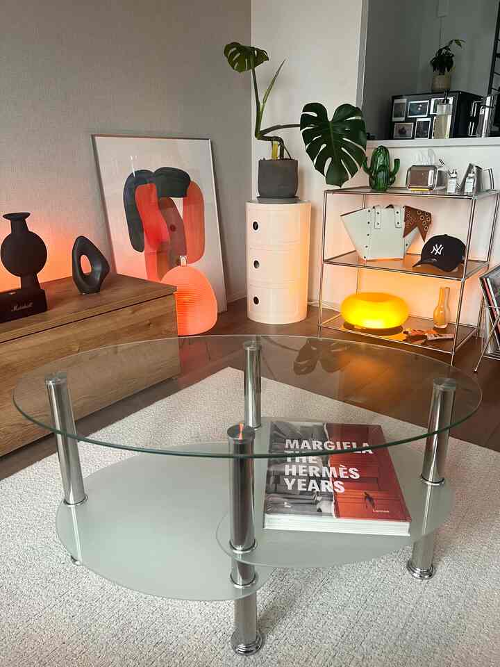 透明なガラステーブルと木目調家具が配置された明るくナチュラルなリビング、間接照明が演出