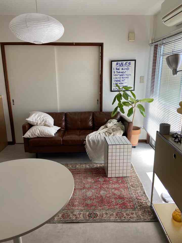 ブラウンレザーソファと白いアクセントが調和する1DKのリビング、ミッドセンチュリーモダンスタイルの温かみのある空間