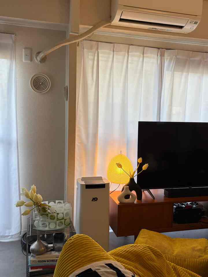 明るい白いカーテンと温かみのある黄色のソファがある1LDKのリビング、自然光と照明で雰囲気のあるインテリア