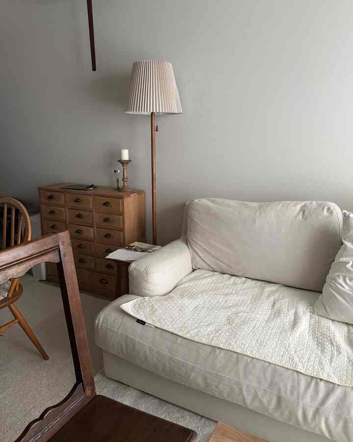 ナチュラルな色調の1LDKリビング、白いソファと木製のフロアランプ、ヴィンテージ風の無垢材家具が配置された落ち着いた空間